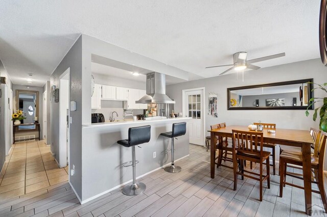 kitchen featuring white cabinets, a breakfast bar area, a peninsula, island exhaust hood, and light countertops