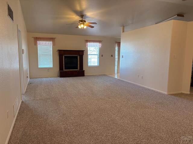 unfurnished living room featuring ceiling fan, a tile fireplace, carpet flooring, visible vents, and baseboards