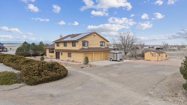 view of side of property featuring driveway, an attached garage, stucco siding, a chimney, and roof mounted solar panels