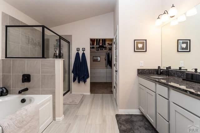 bathroom featuring lofted ceiling, a spacious closet, a stall shower, vanity, and a bath