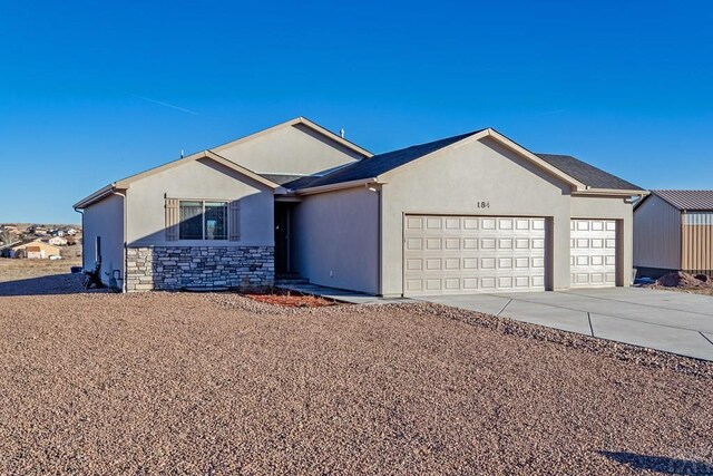 single story home with an attached garage, stone siding, driveway, and stucco siding