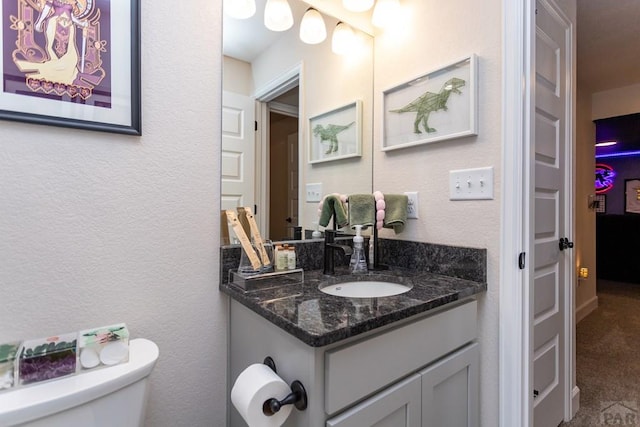 bathroom with toilet, a textured wall, and vanity