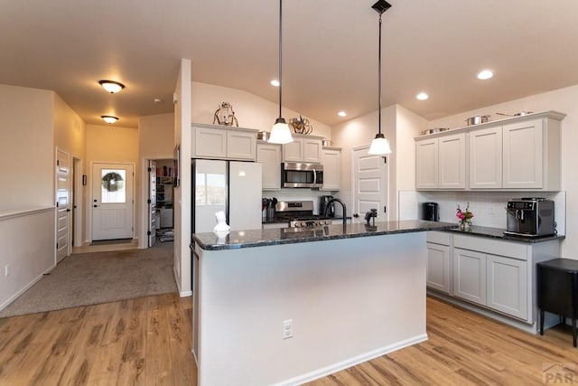 kitchen featuring tasteful backsplash, light wood-style flooring, dark stone countertops, hanging light fixtures, and stainless steel appliances