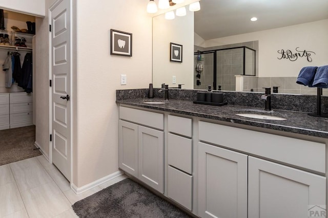 bathroom with a walk in closet, a sink, a shower stall, and double vanity