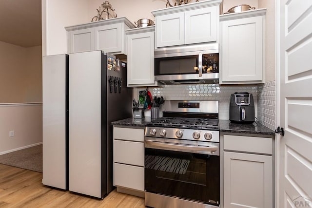 kitchen with light wood finished floors, appliances with stainless steel finishes, white cabinets, and backsplash