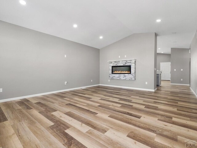 unfurnished living room featuring lofted ceiling, recessed lighting, light wood-style flooring, a glass covered fireplace, and baseboards