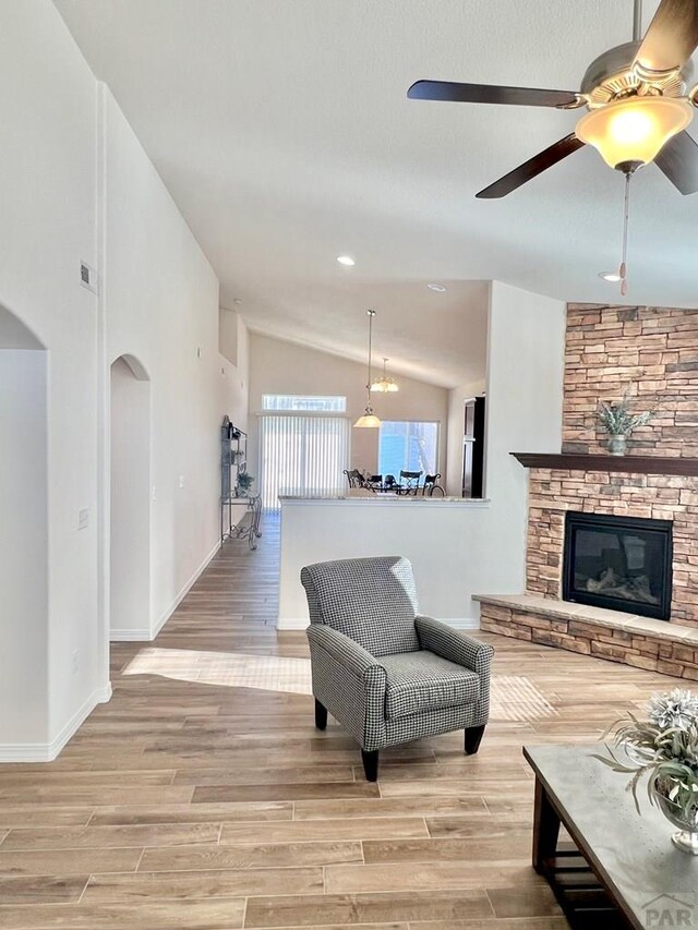 living room featuring light wood-type flooring, a fireplace, arched walkways, and lofted ceiling