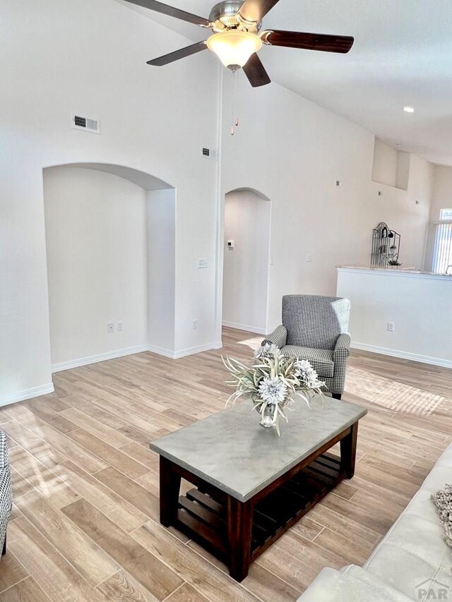 living area with light wood-type flooring, visible vents, arched walkways, and baseboards