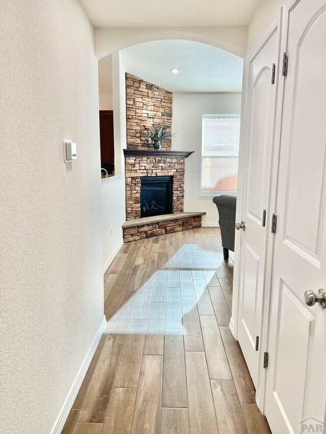 hall with a textured wall, baseboards, arched walkways, and wood finish floors