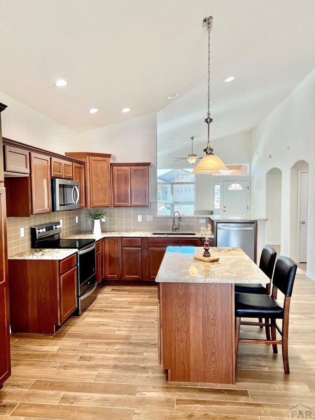 kitchen featuring arched walkways, a kitchen island, a kitchen breakfast bar, stainless steel appliances, and a sink