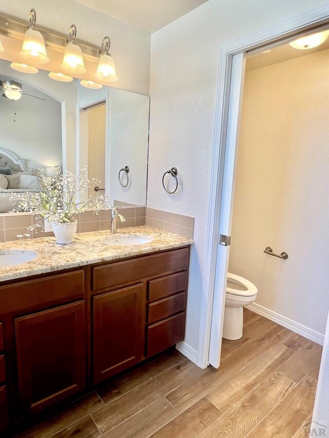 ensuite bathroom featuring double vanity, baseboards, toilet, wood finished floors, and a sink