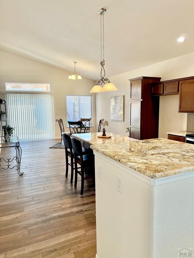 kitchen featuring decorative light fixtures, light wood finished floors, lofted ceiling, brown cabinetry, and light stone countertops