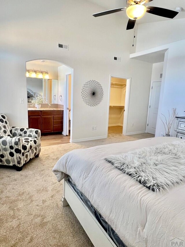 bedroom featuring baseboards, arched walkways, ensuite bathroom, a spacious closet, and high vaulted ceiling