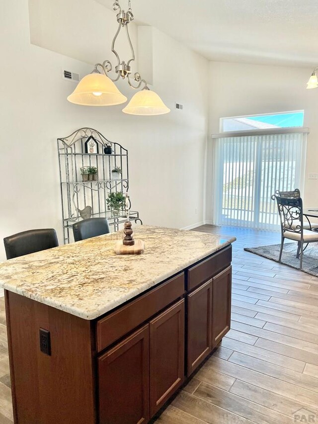 kitchen featuring visible vents, lofted ceiling, light wood-style flooring, a kitchen island, and hanging light fixtures