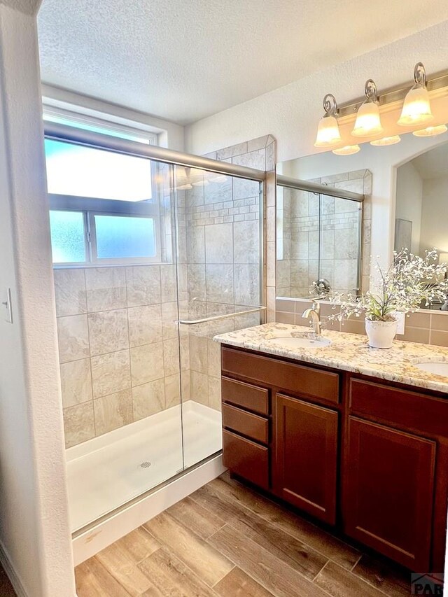 full bath featuring a shower stall, a textured ceiling, wood finished floors, and vanity