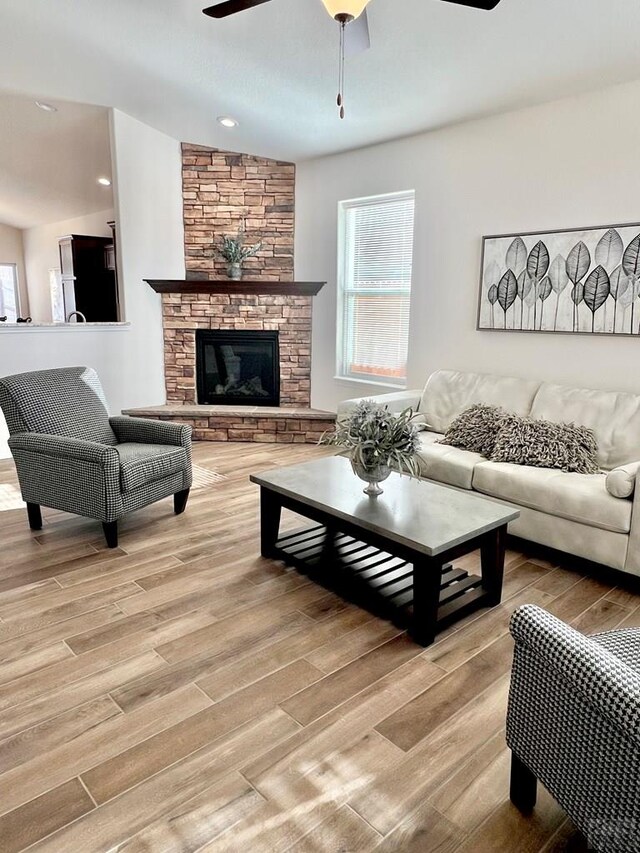 living room with ceiling fan, a stone fireplace, and light wood-style floors