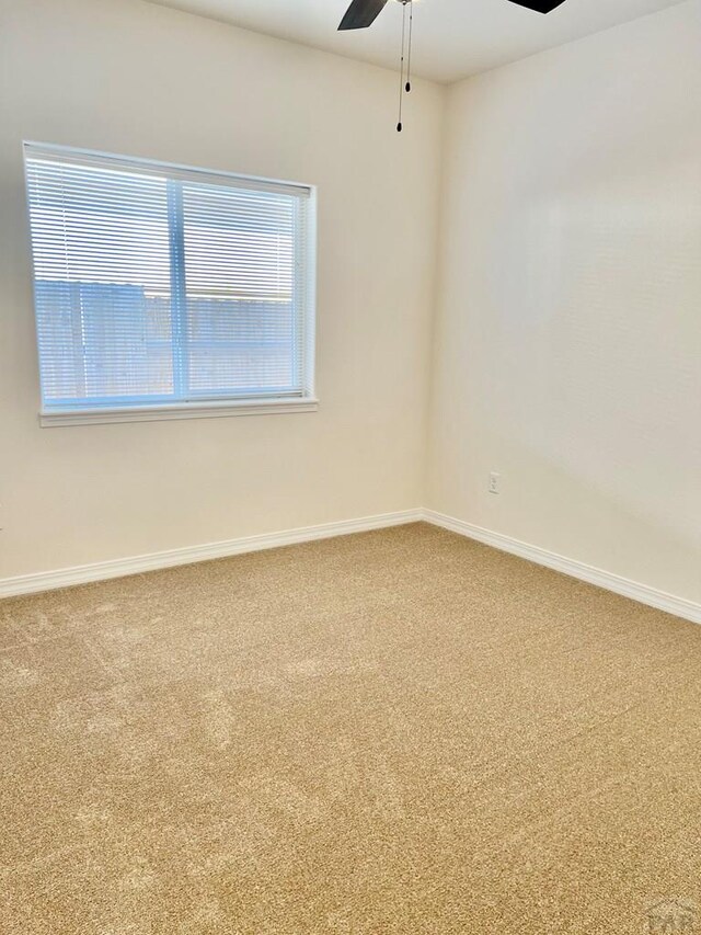 carpeted spare room with a ceiling fan and baseboards