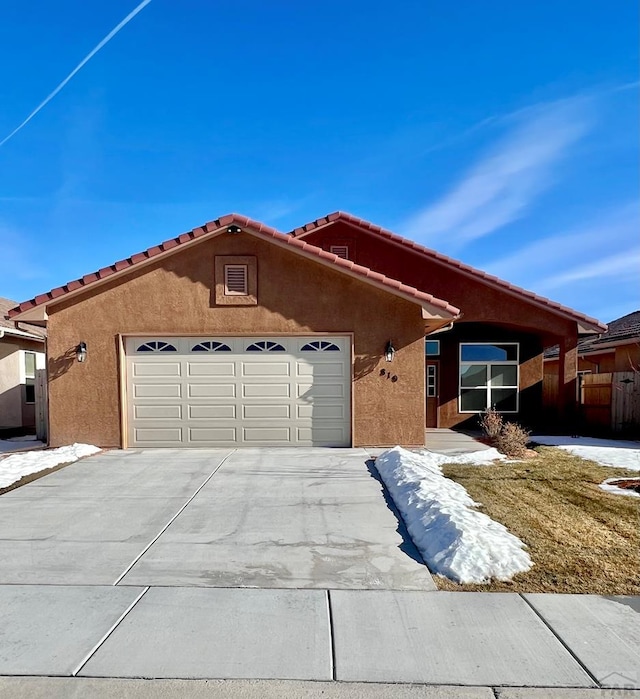 view of front of home featuring driveway, a tiled roof, a garage, and stucco siding