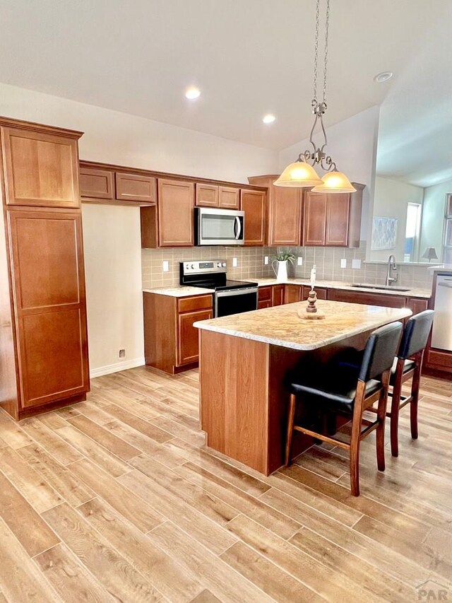 kitchen with stainless steel appliances, a sink, a center island with sink, and brown cabinets