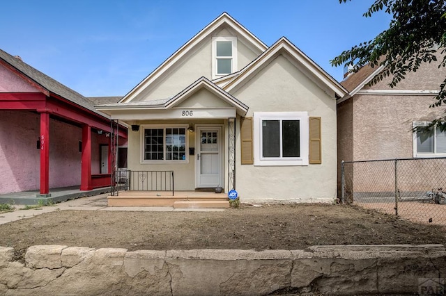 bungalow-style house with fence, covered porch, and stucco siding