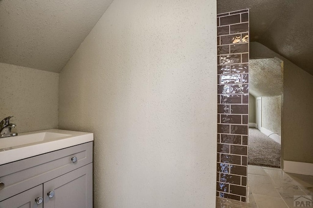 bathroom featuring a textured ceiling, vanity, a textured wall, and vaulted ceiling