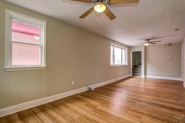 empty room with visible vents, baseboards, stairway, light wood-style flooring, and a ceiling fan