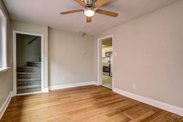 unfurnished room featuring stairway, a ceiling fan, baseboards, and light wood finished floors