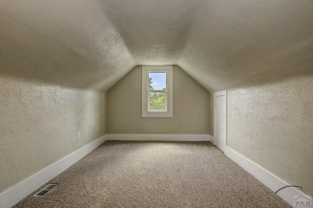 bonus room featuring visible vents, a textured ceiling, carpet floors, lofted ceiling, and a textured wall