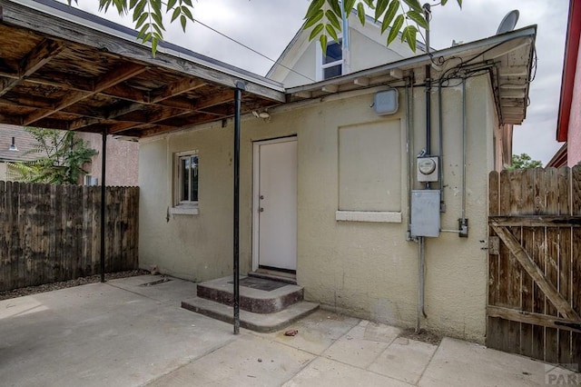 entrance to property with a patio area, fence, and stucco siding