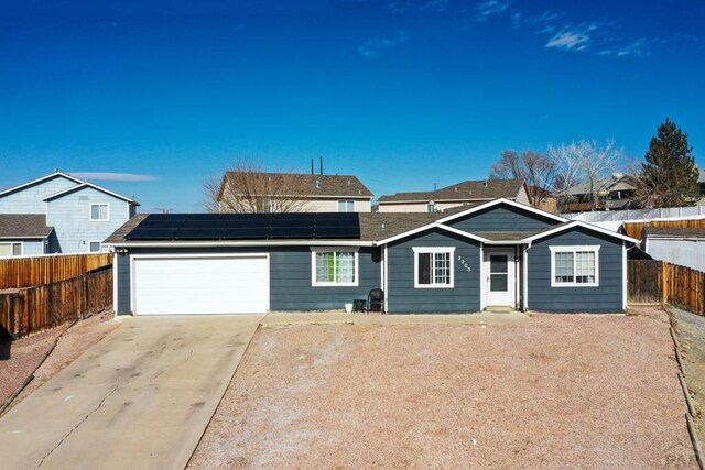 ranch-style house featuring a garage, roof mounted solar panels, fence, and concrete driveway