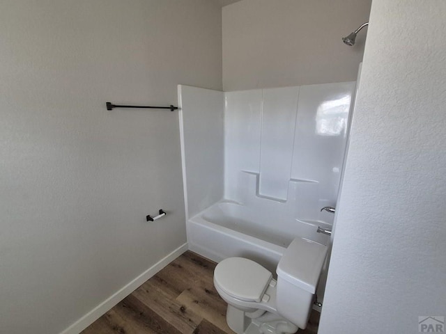 bathroom featuring baseboards, shower / tub combination, toilet, and wood finished floors