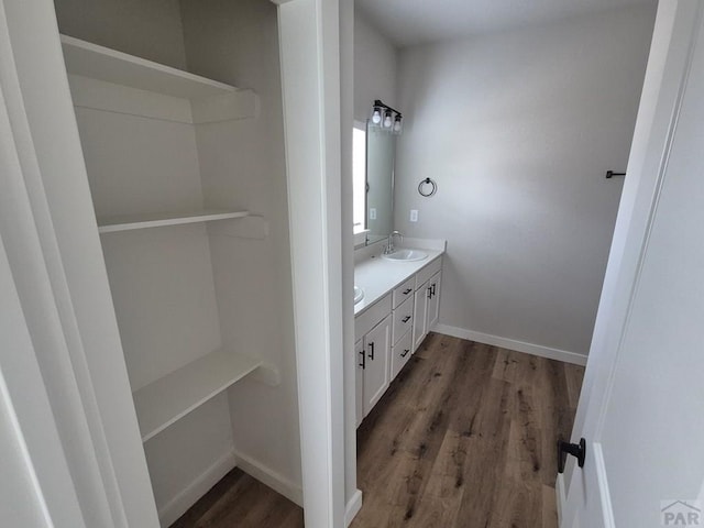 full bathroom with double vanity, wood finished floors, a sink, and baseboards