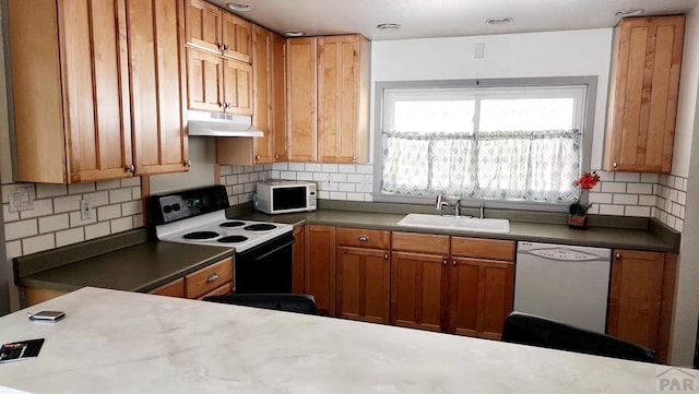 kitchen featuring white appliances, under cabinet range hood, backsplash, and a sink