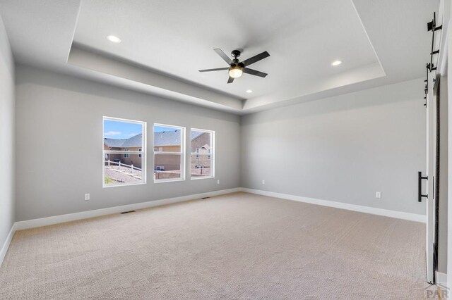 empty room with light carpet, a tray ceiling, and baseboards