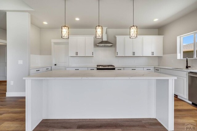 kitchen featuring wall chimney exhaust hood, hanging light fixtures, a kitchen island, and white cabinets