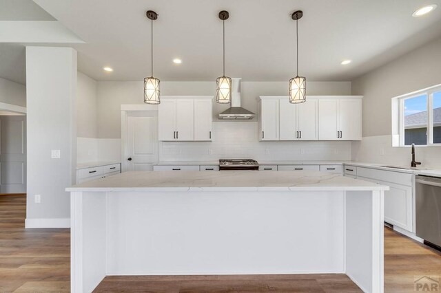 kitchen with wall chimney exhaust hood, light stone counters, a center island, stainless steel appliances, and white cabinetry