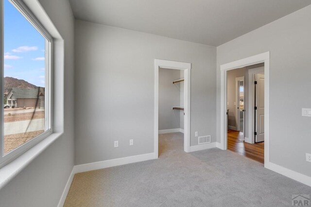 unfurnished bedroom with light carpet, a spacious closet, visible vents, and baseboards