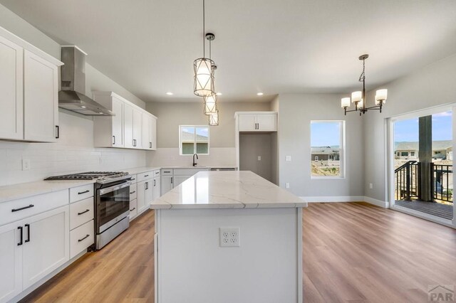 kitchen featuring hanging light fixtures, white cabinets, a kitchen island, wall chimney range hood, and stainless steel gas range