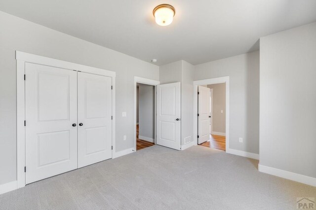 unfurnished bedroom featuring a closet, light colored carpet, and baseboards