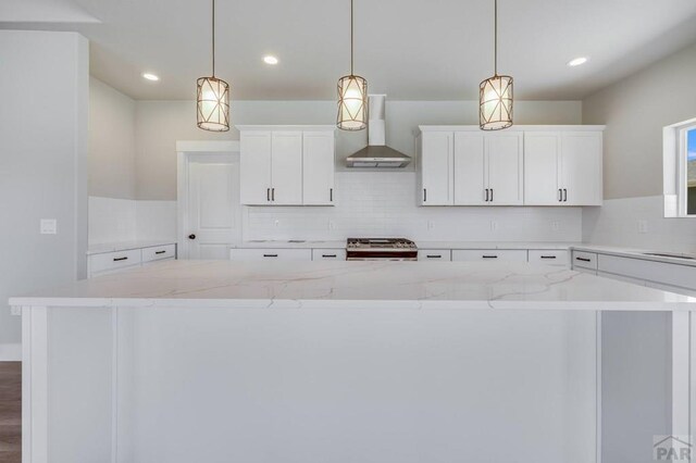 kitchen with wall chimney exhaust hood, a kitchen island, stove, hanging light fixtures, and white cabinetry