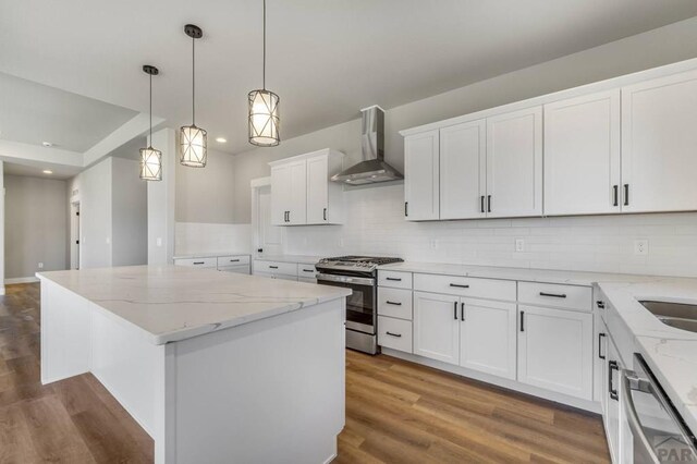 kitchen featuring a center island, hanging light fixtures, appliances with stainless steel finishes, white cabinets, and wall chimney range hood