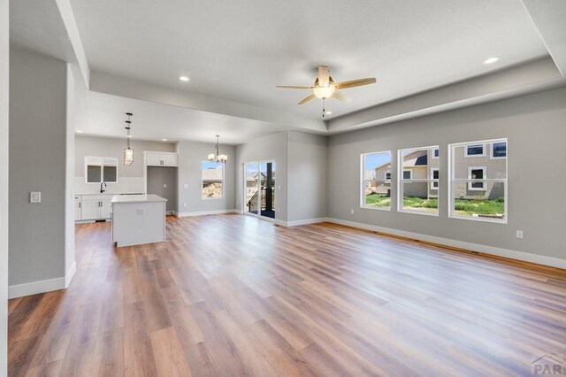 unfurnished living room with recessed lighting, light wood-style flooring, baseboards, and ceiling fan with notable chandelier