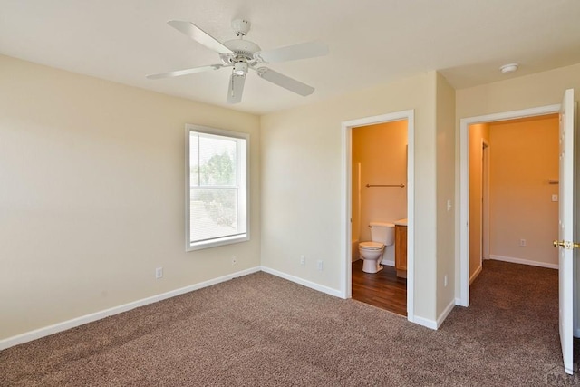 unfurnished bedroom featuring ceiling fan, dark carpet, connected bathroom, and baseboards