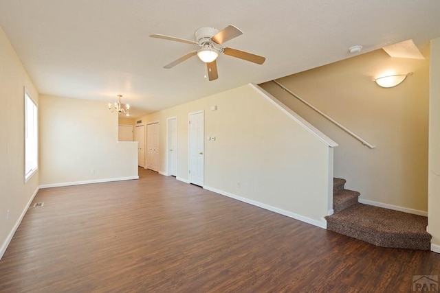 unfurnished living room featuring ceiling fan with notable chandelier, dark wood-style flooring, baseboards, and stairs