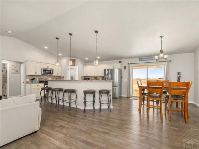 kitchen featuring appliances with stainless steel finishes, a kitchen breakfast bar, dark wood-style flooring, vaulted ceiling, and white cabinetry