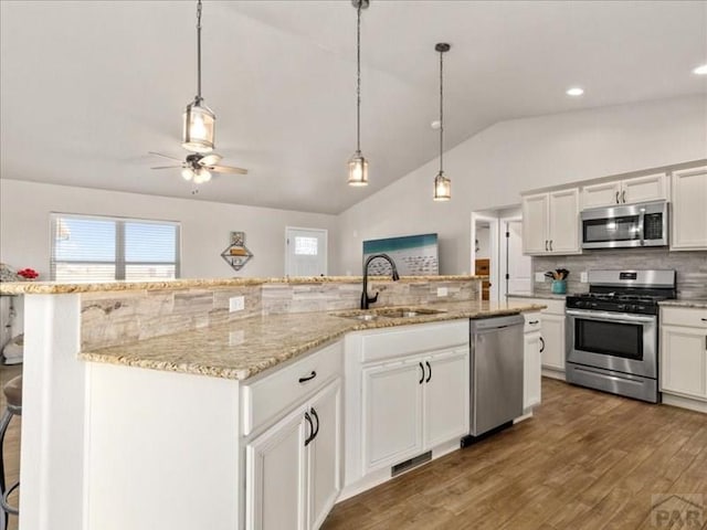 kitchen with a center island with sink, appliances with stainless steel finishes, wood finished floors, a sink, and backsplash