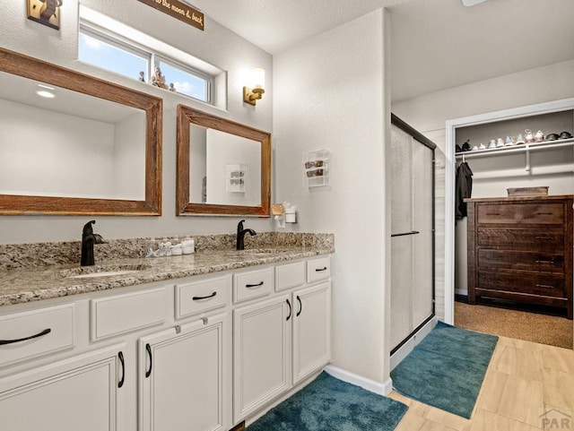 bathroom featuring baseboards, double vanity, a sink, and a shower stall