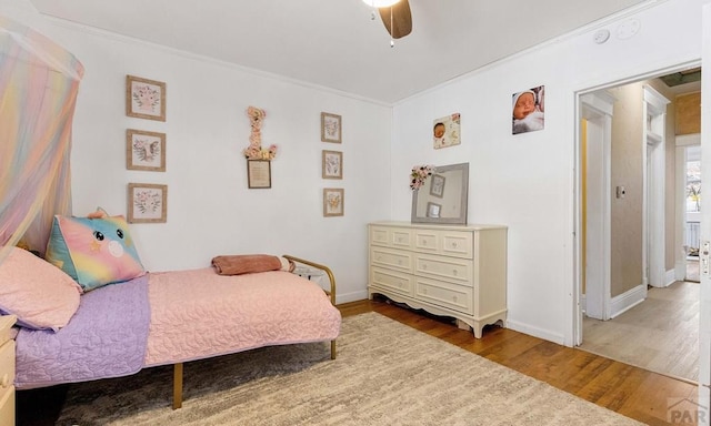 bedroom featuring a ceiling fan, crown molding, baseboards, and wood finished floors