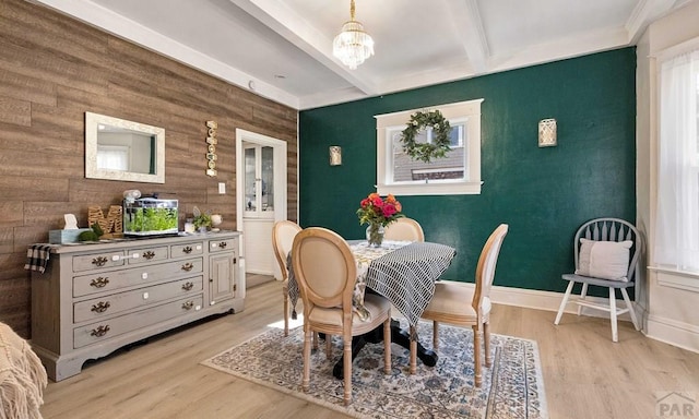 dining room featuring an accent wall, beam ceiling, light wood-type flooring, and an inviting chandelier