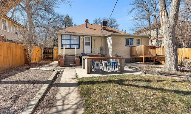 back of house with a wooden deck, a fenced backyard, a shingled roof, a chimney, and a patio area